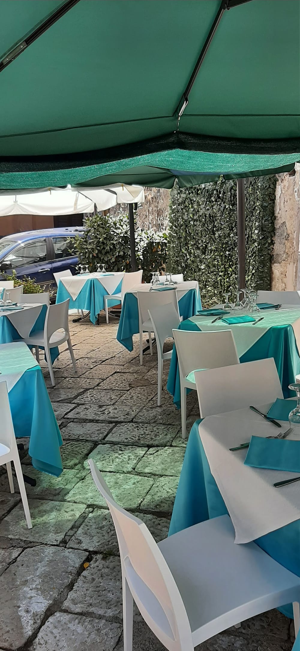 Il cortile del Cambusone in Piazza Sant'Andrea: tavoli con tovaglie turchesi sotto gli ombrelloni verdi, sulle basole di pietra